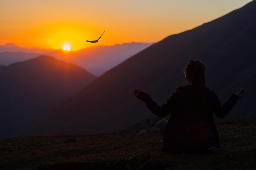Eine Frau in Sillhouette bei Sonnenuntergang vor einem weit entfernten riesigem Berg führt eine Einschlafmeditation durch
