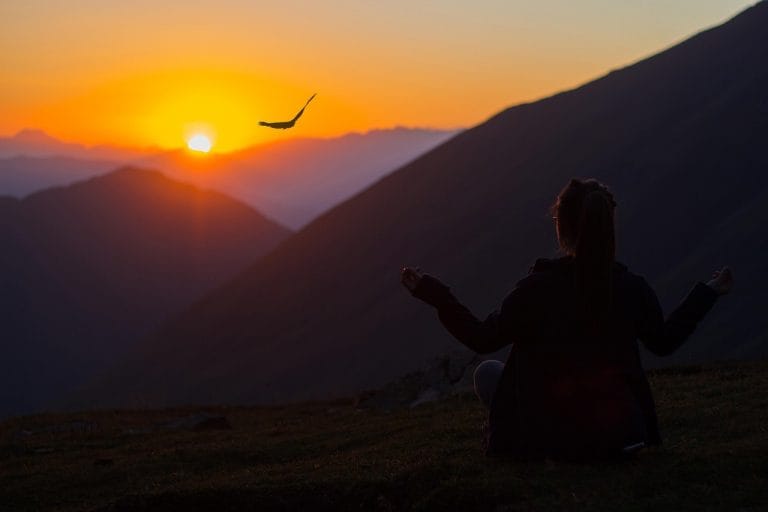Eine Frau in Sillhouette bei Sonnenuntergang vor einem weit entfernten riesigem Berg führt eine Einschlafmeditation durch